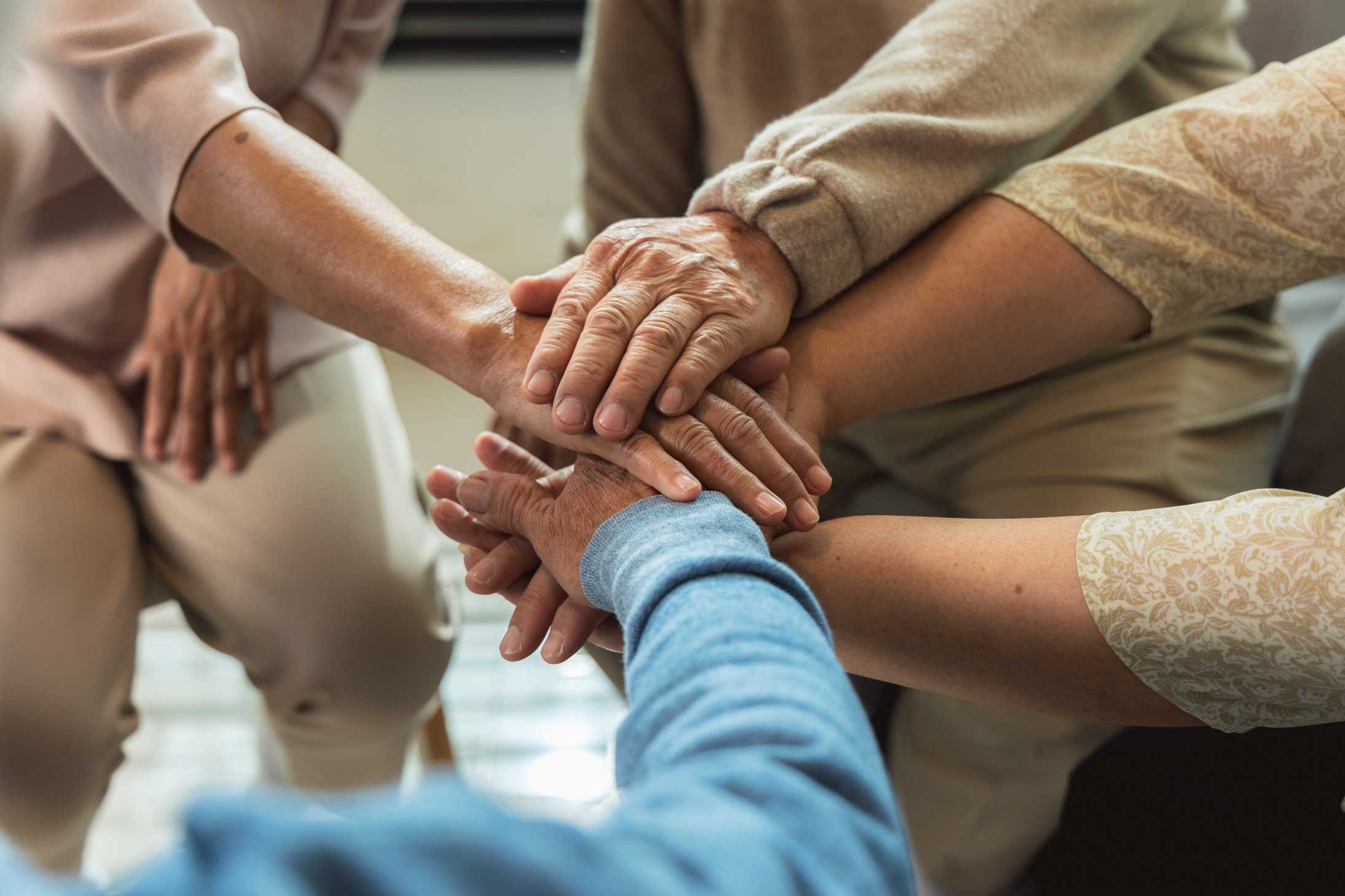 Senior group sitting in a circle with hands stacked together in the center.