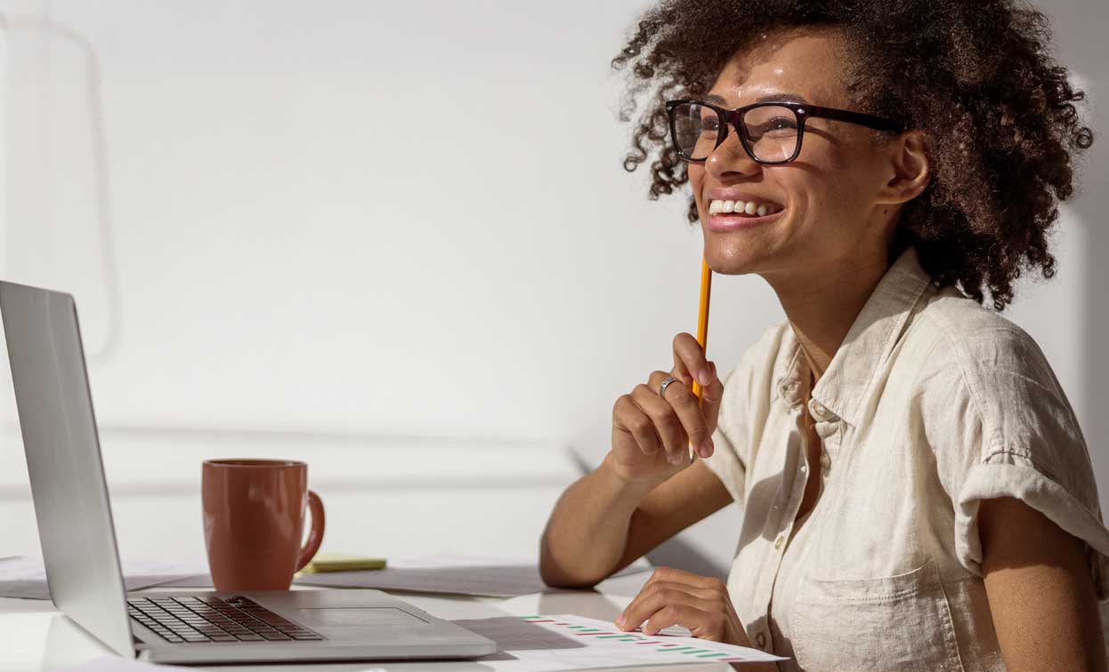 Smiling woman sitting at a desk with pencil in hand with laptop.